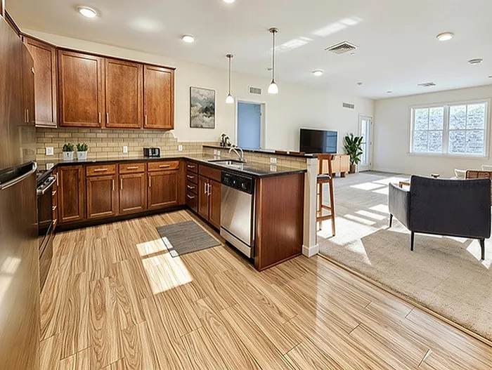 Contemporary open-concept kitchen and living space with elegant wood flooring, stylish pendant lighting, and warm cabinetry.