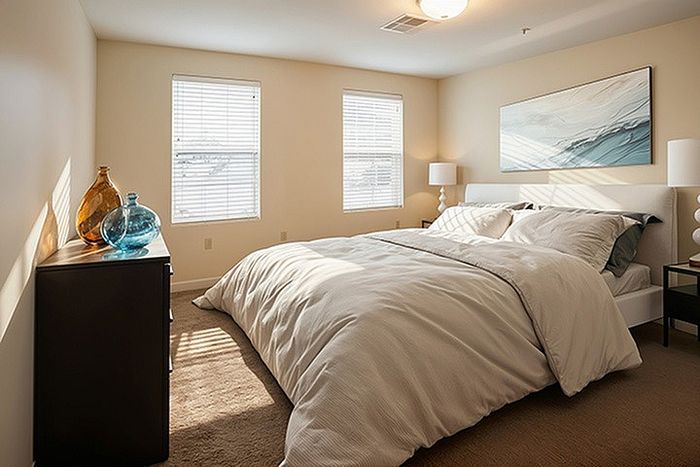 Inviting bedroom with cozy ambiance, featuring plush bedding, elegant artwork, and abundant natural light from large windows.