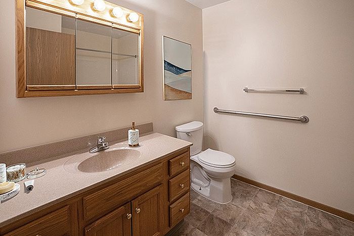 Modern bathroom featuring a sleek wooden vanity with ample storage, elegant countertop, and ambient lighting. The serene design includes a spacious mirror and stylish wall art, creating a tranquil retreat.