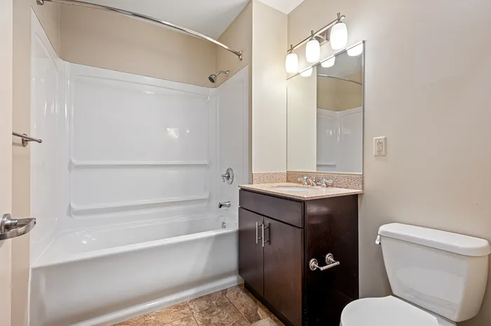 Modern bathroom featuring a sleek bathtub, elegant vanity with granite countertop, and stylish lighting fixtures.
