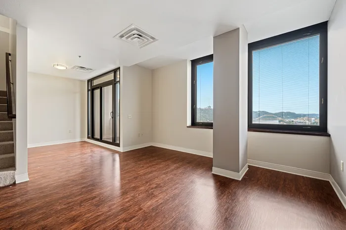Bright and airy living space with elegant hardwood floors, large windows offering stunning views, and a glass door leading to an outdoor area.