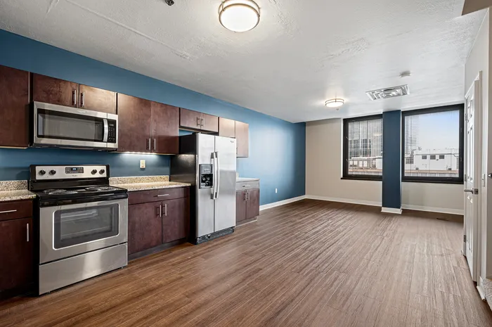 Modern kitchen with stainless steel appliances, sleek cabinetry, and an open layout leading to a spacious living area featuring large windows with city views.