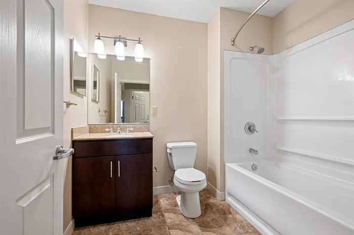 Sleek modern bathroom featuring a polished granite vanity, elegant dark wood cabinetry, and a pristine shower-tub combination for ultimate relaxation.