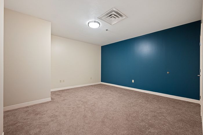 Spacious room with modern lighting, plush carpet, and a stylish blue accent wall.