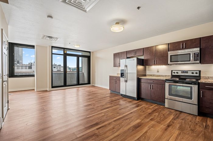 Modern open-concept apartment with sleek kitchen appliances, hardwood floors, and stunning city views through large windows.