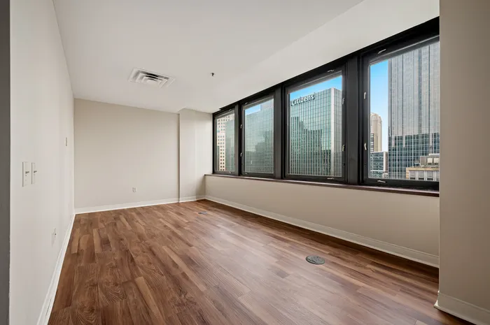 Bright city apartment room featuring polished wood floors and expansive windows with skyline view.
