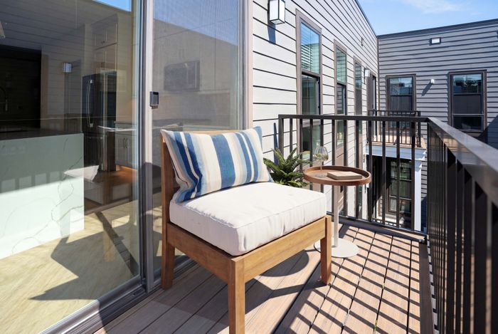 Chic apartment balcony featuring a cozy wooden chair with a stylish striped cushion, accented by a modern side table and elegant glass railing.