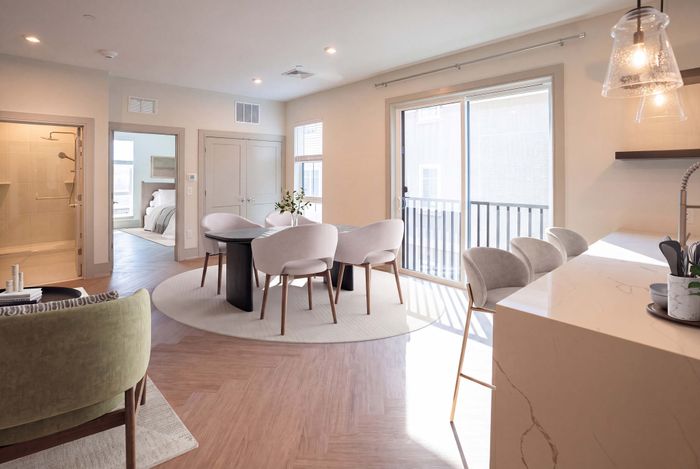 Bright, modern apartment interior with elegant dining area, cozy living space, and sleek kitchen, all bathed in natural light from large sliding glass doors.