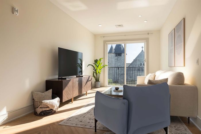 Bright and elegant living room with a cozy sofa, sleek TV setup, and French doors opening to a picturesque view, accented by stylish decor and abundant natural light.