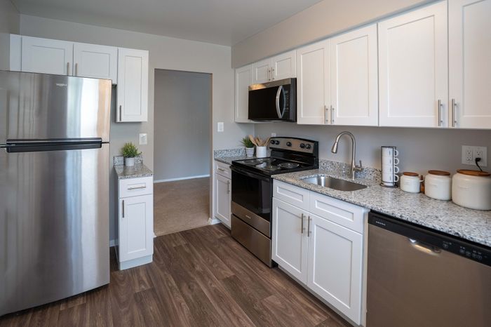 Modern kitchen with sleek stainless steel appliances, elegant white cabinetry, and granite countertops, featuring warm wood flooring and stylish decor.