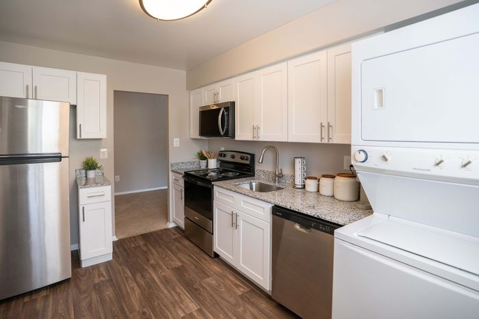 Modern kitchen with sleek white cabinets, stainless steel appliances, and granite countertops, complete with in-unit laundry.