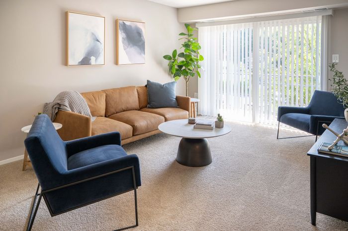 Bright and inviting living room featuring a cozy beige sofa, stylish blue chairs, and modern decor, with natural light streaming through large windows.