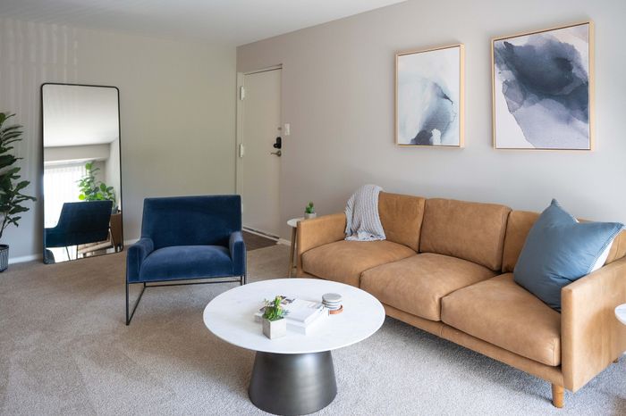 Modern living room with stylish tan sofa, plush blue armchair, and chic marble coffee table, perfect for relaxing and entertaining.