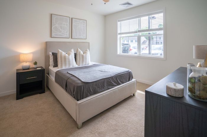 Bright and cozy bedroom with stylish decor, plush carpeting, and ample natural light through large windows.