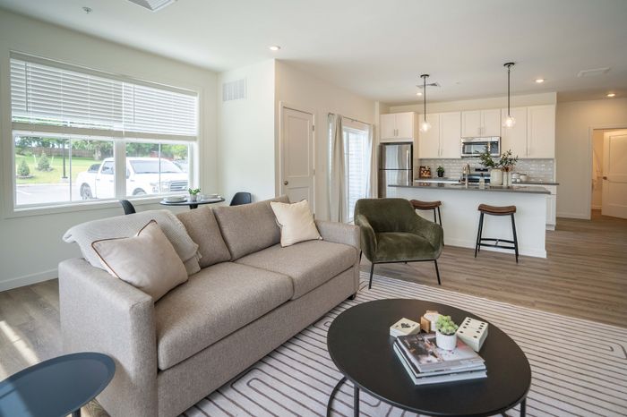 Modern open-plan living area boasting a cozy sofa, elegant kitchen with bar stools, and natural light from large windows.