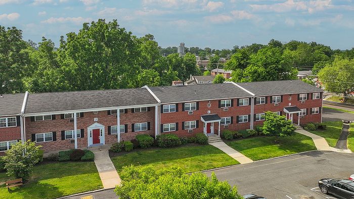 Charming brick apartment complex surrounded by lush greenery, featuring well-maintained lawns and inviting entrances.