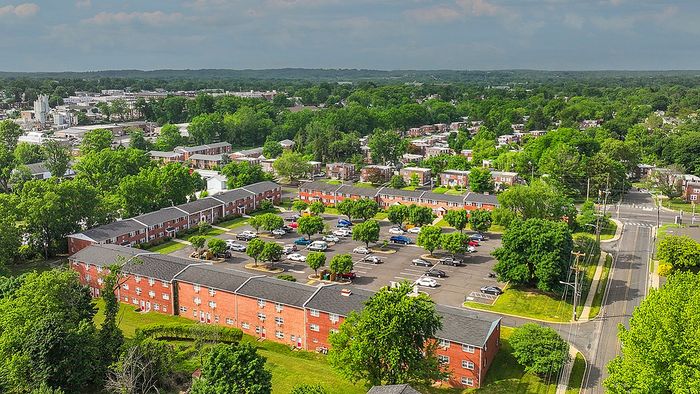Charming aerial view of a vibrant apartment complex surrounded by lush greenery, with ample parking and scenic neighborhood vistas.
