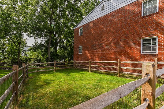Charming corner of a brick home with a lush fenced garden, offering a serene outdoor space surrounded by vibrant greenery.