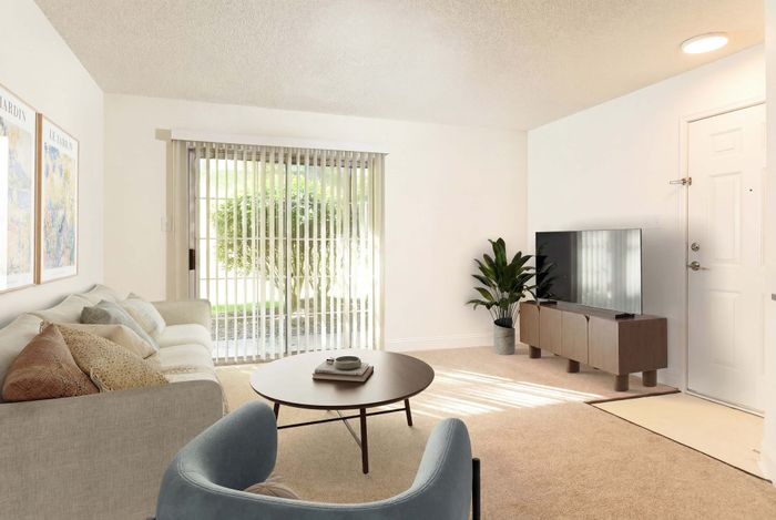 Bright living room with a cozy beige sofa, elegant coffee table, and modern TV setup, accented by greenery and large sliding glass doors.