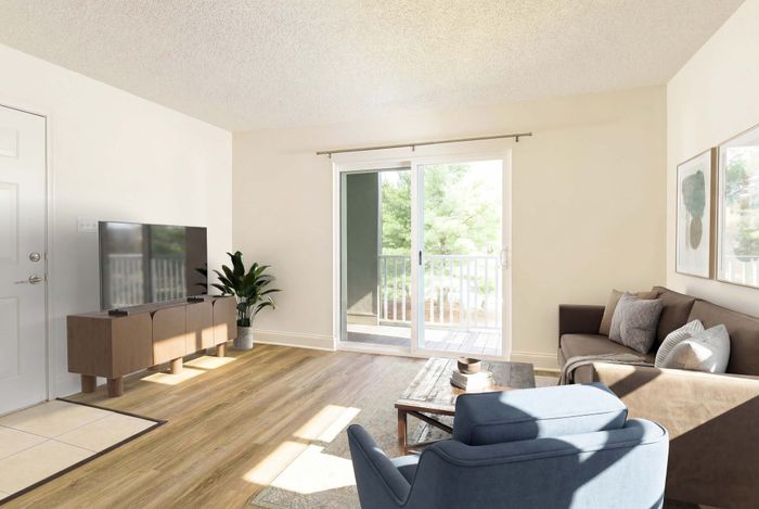Inviting living room with large glass doors opening to a balcony, featuring cozy brown and blue seating, modern TV setup, and abundant natural light.