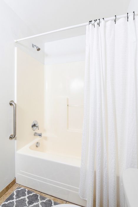 Modern bathroom featuring a pristine shower-tub combo with elegant white curtains and stylish tiled flooring.