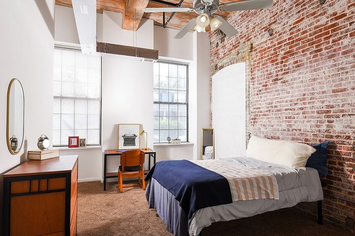 Chic urban bedroom with exposed brick wall, cozy bed, stylish desk, and modern decor, creating a welcoming and trendy living space.