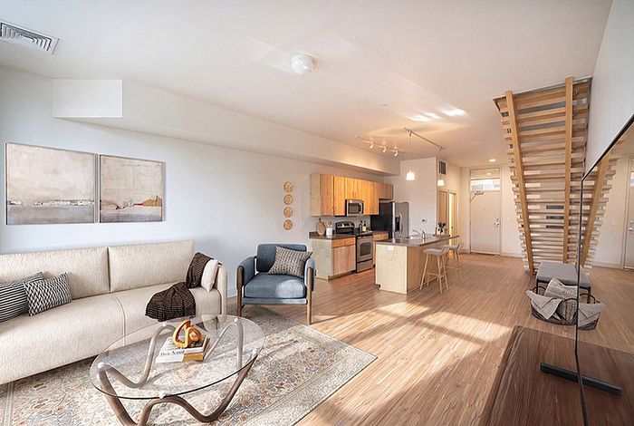 Open-concept living space featuring modern kitchen, cozy seating area, and elegant wooden staircase, filled with natural light.