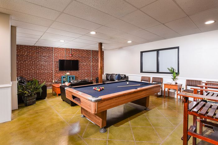 Chic apartment recreation room featuring a stylish pool table, inviting seating area, and modern brick accent wall.