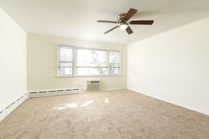 Bright and spacious living room with plush carpeting, large windows for natural sunlight, and a stylish ceiling fan, perfect for a cozy home environment.