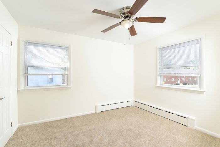 Bright and airy bedroom with plush carpeting, large windows for natural light, and a modern ceiling fan.