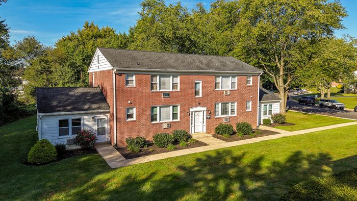 Charming brick apartment building with manicured lawns and lush green surroundings, perfect for peaceful living.