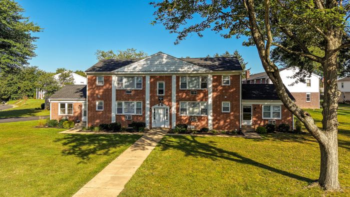 Charming brick apartment complex with a classic design, surrounded by lush greenery and a welcoming pathway.