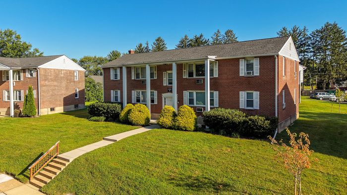 Charming two-story red brick apartment complex surrounded by lush greenery and vibrant landscaping.