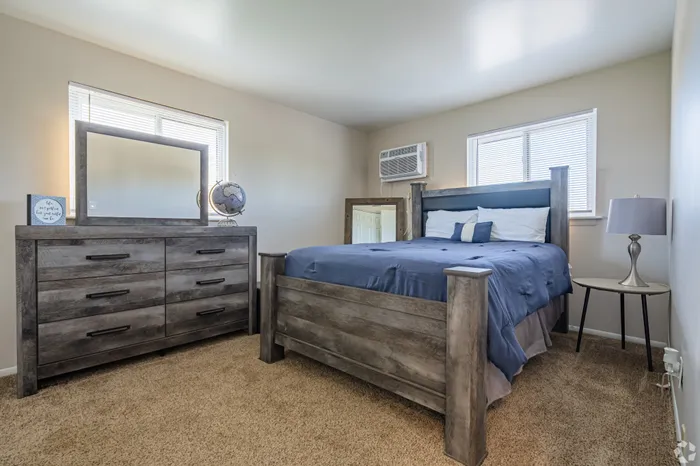 Inviting bedroom with a cozy atmosphere, featuring a stylish wooden bed frame, elegant dresser with mirror, and plush carpet flooring.