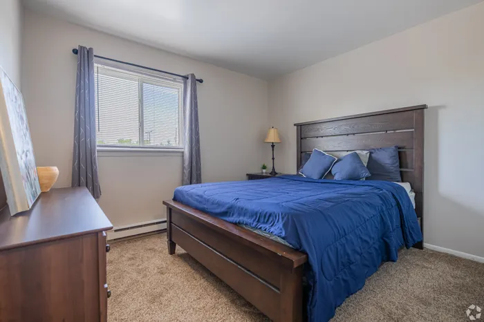 Inviting bedroom with plush carpeting, rich wooden furniture, and ample natural light from a large window.