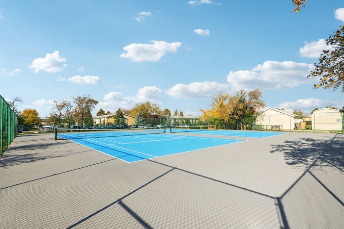 Sunlit tennis courts at a vibrant residential community, surrounded by lush greenery and clear blue skies.