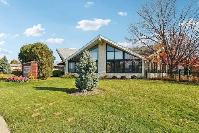 Charming brick building with a contemporary architectural design, surrounded by lush green lawns and vibrant autumn trees, under a clear blue sky.