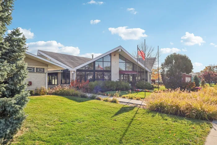 Charming brick building with large glass windows, surrounded by lush greenery and a beautifully maintained lawn, under a clear blue sky.
