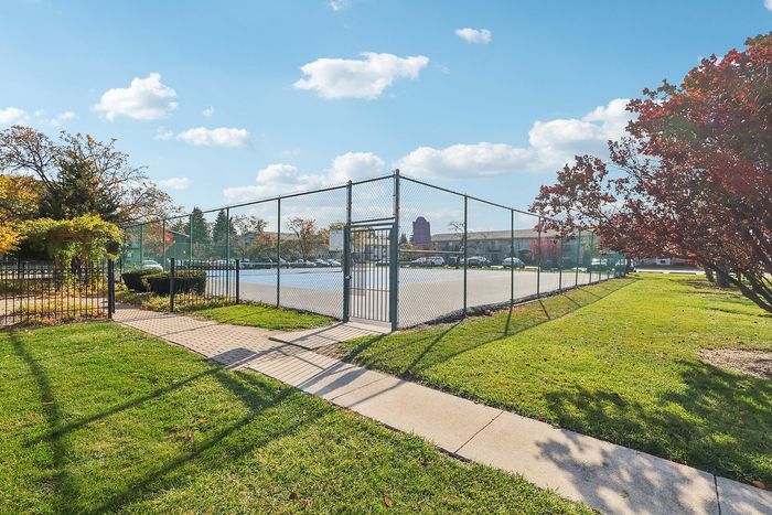 Inviting community tennis court surrounded by lush greenery and a clear blue sky, perfect for outdoor sports enthusiasts.