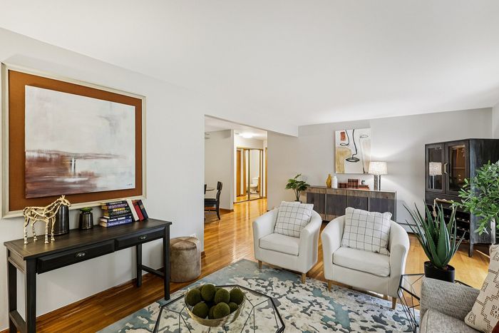 Elegant living room with modern decor, featuring plush white armchairs, stylish artwork, and a cozy seating area on polished hardwood floors.