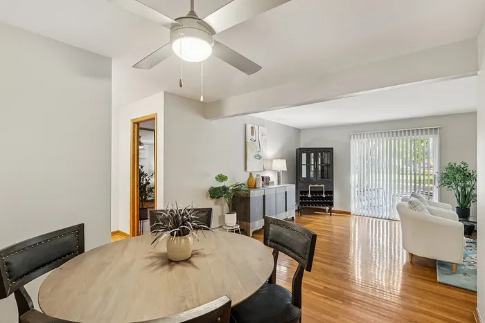 Charming open-concept living and dining area showcasing elegant wood flooring, a stylish ceiling fan, and abundant natural light from large windows.