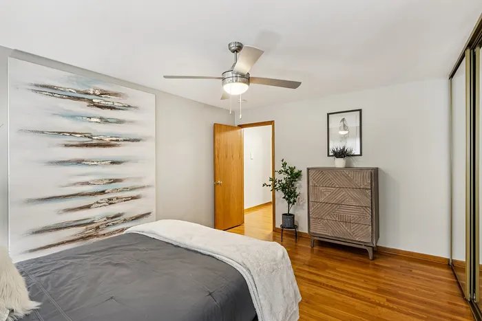 Inviting bedroom with modern ceiling fan, stylish decor, and warm wooden flooring.