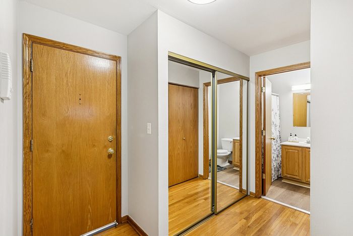 Bright entryway with elegant wooden doors and mirrored closet reflecting a sleek bathroom, showcasing modern style and functionality.