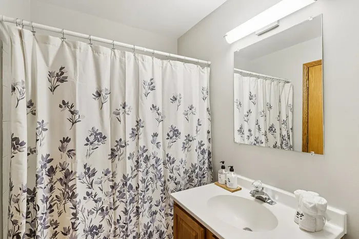 Charming bathroom with floral shower curtain and elegant vanity mirror, creating a cozy and inviting atmosphere.