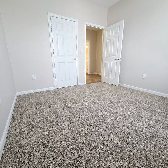 Bright bedroom with plush carpeting, neutral walls, and modern double doors, offering a cozy and inviting atmosphere.