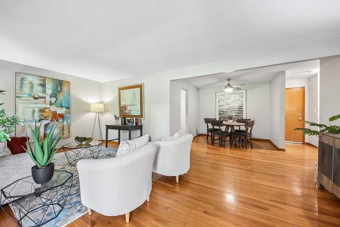 Elegant open-concept living and dining area with stylish furnishings, vibrant artwork, and abundant natural light on polished hardwood floors.