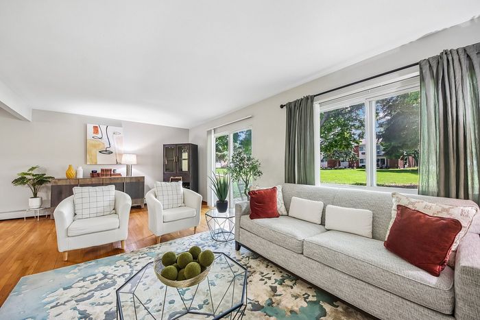 Bright and inviting living room with modern decor, featuring large windows overlooking lush greenery, a comfortable gray sofa, and stylish armchairs.