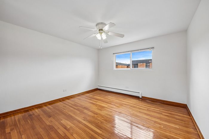 Bright and inviting empty room with polished hardwood floors and a ceiling fan, perfect for customization.