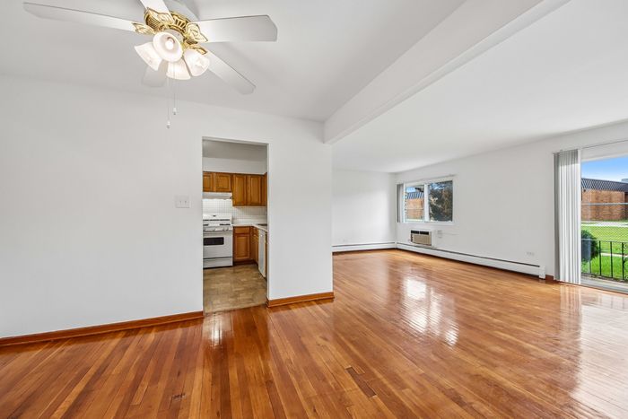 Bright, spacious apartment with gleaming hardwood floors, a cozy kitchen with wooden cabinets, and a sunlit living room opening to a lush outdoor view.