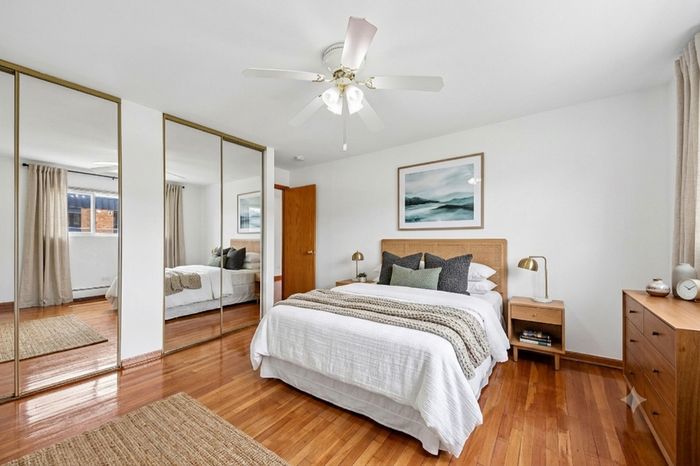 Elegant bedroom with polished hardwood floors, mirrored closet doors, and cozy decor, featuring a plush bed, stylish nightstands, and natural light filtering through large windows.